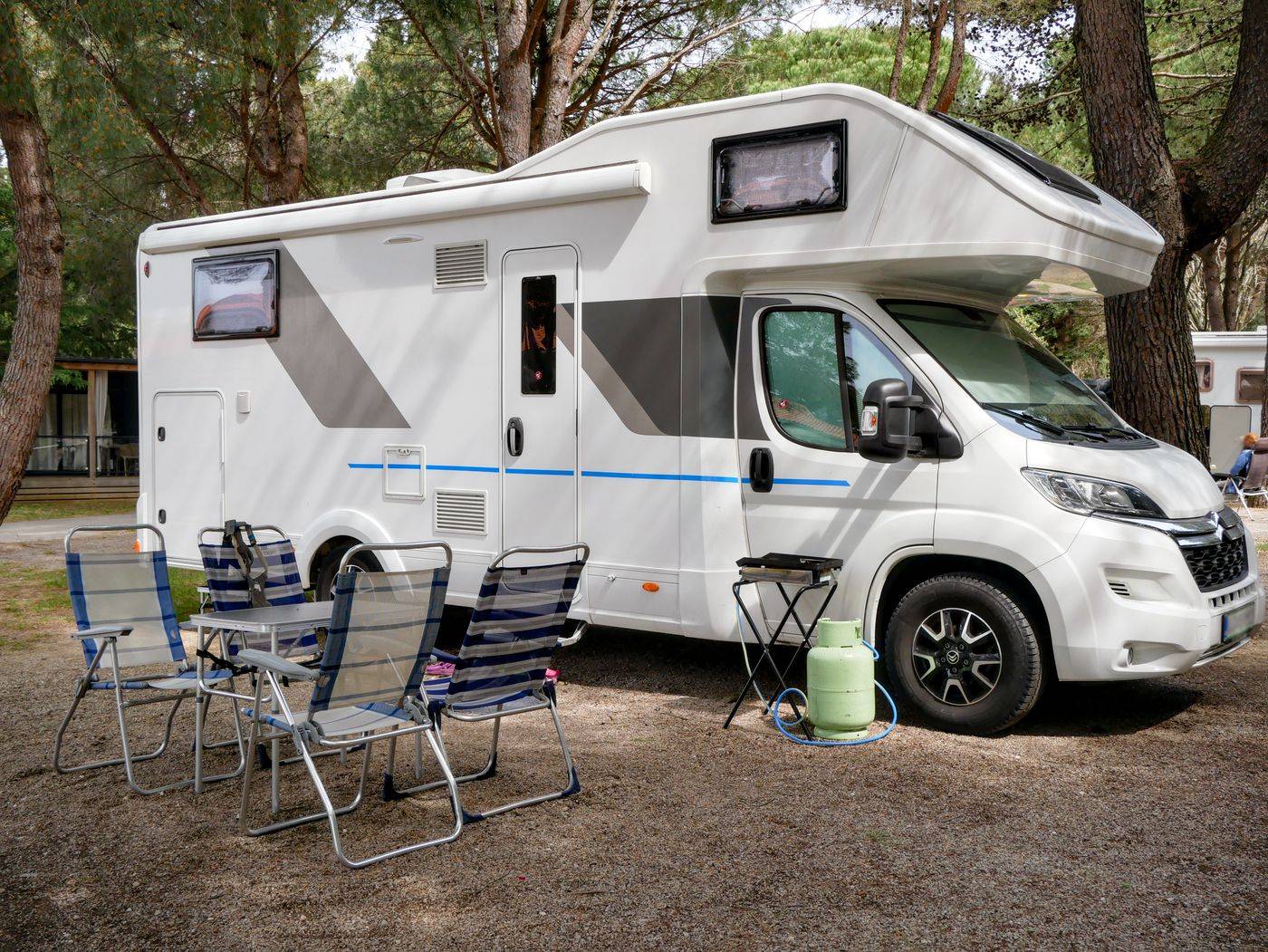 A motorhome parked at a forest campsite with camp chairs set out